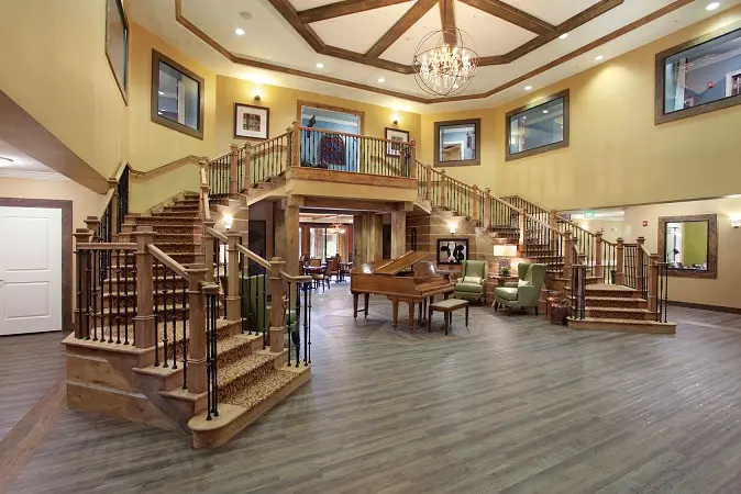 Main entryway with dual staircase and walnut colored piano in Wildwood senior living community.