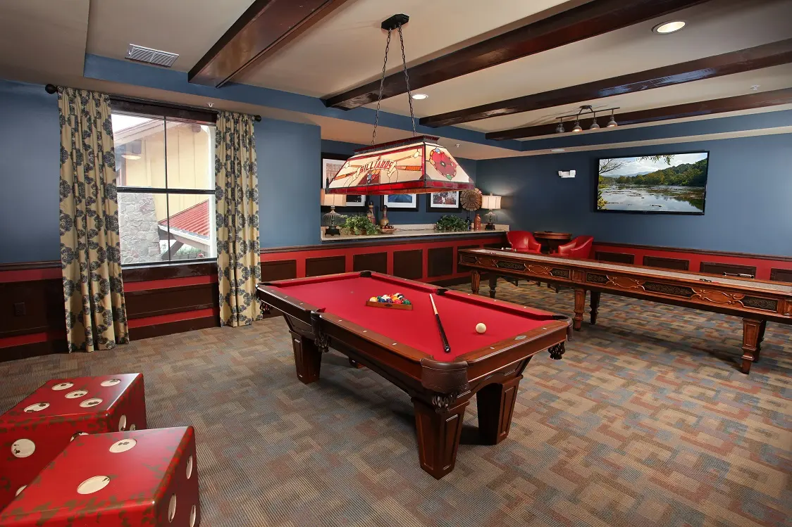 A game room with a red billiard table and a shuffle board table in Wildwood retirement home.