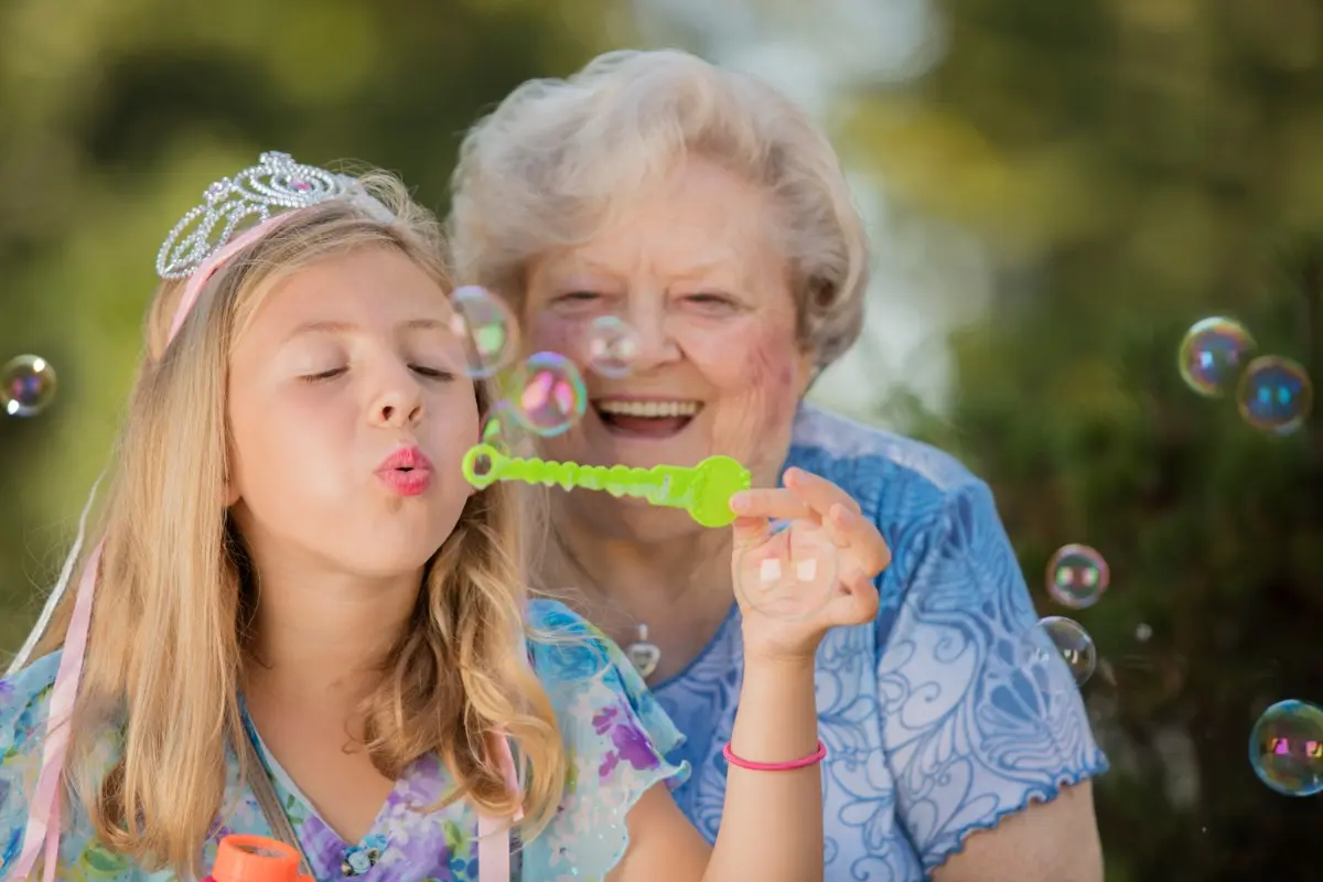 Senior citizen woman blowing bubbles with grandchild American House Milford adsf