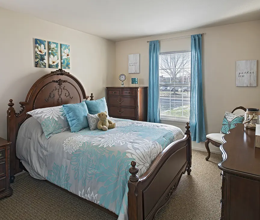 Senior apartment bedroom with blue bed covers and drapes and a teddy bear on the bed in Troy, MI