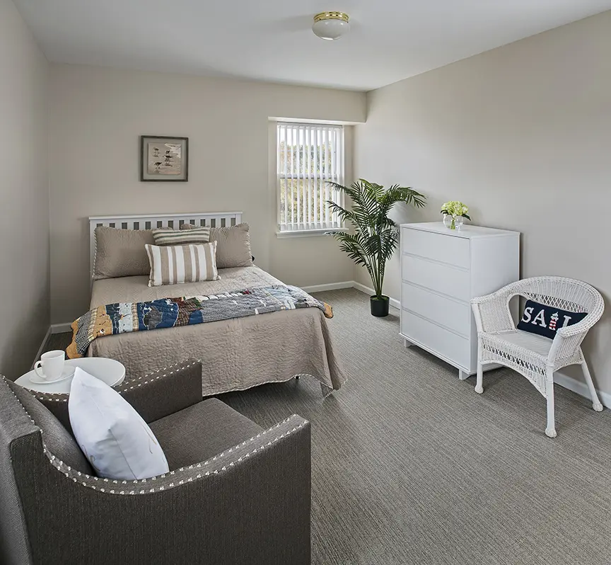 Bedroom with two chairs and a bed with brown covers in a senior housing apartment in Rochester Hills, MI