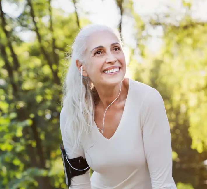 A senior citizen woman smiling doing physical activity, wearing earbuds